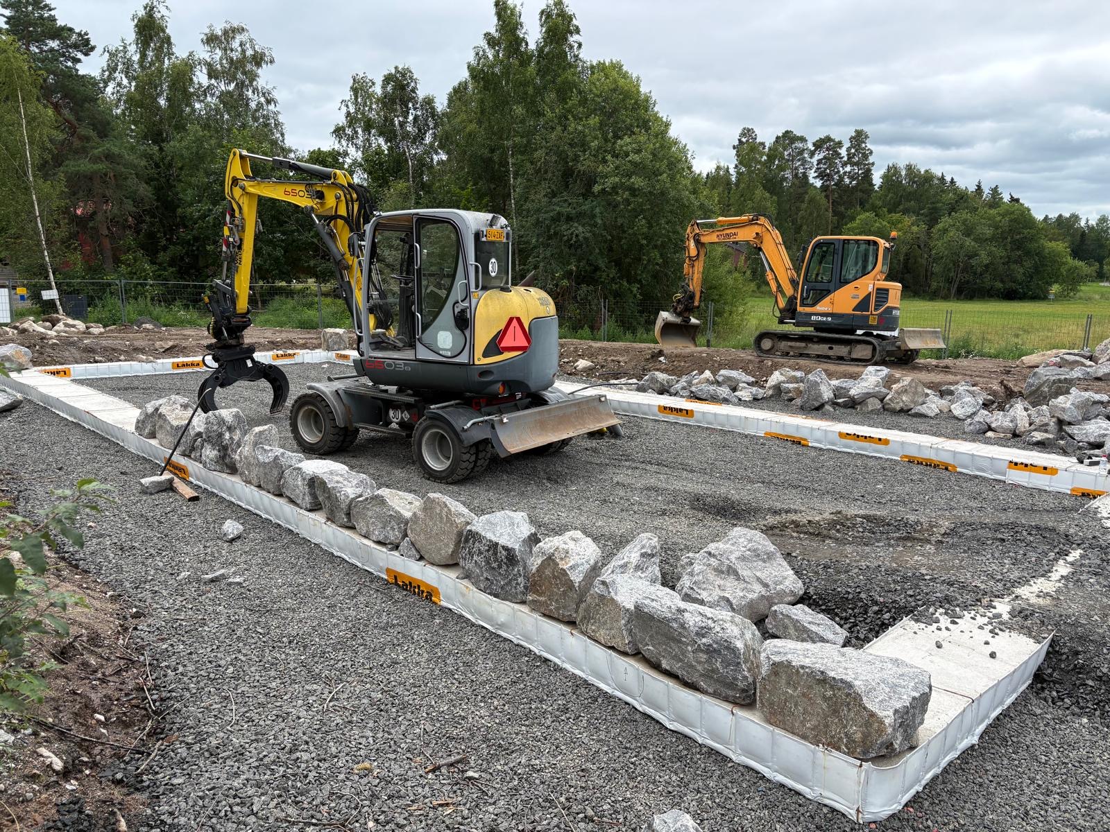19.7.2026 Pihkalan kivisokkelin latominen. Sokkeli rakennetaan perinteiseen tapaan kylmäladontana, jonka jälkeen saumat muurataan kalkkisementtilaastilla. Sokkeli ladotaan tontilla louhitusta kivestä!